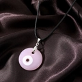 Close-up of a pink resin Evil Eye pendant with a black cord on brown silk fabric - Pink