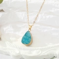 Detail van een gouden ketting met een blauwe druppelkristal en natuurlijke minerale textuur - Teal Waterdruppel (6)