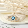 Vintage gold devil eye necklace with blue center and sparkling crystals on stone background - Hollow Eye Style