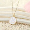 Close-up of golden smiley face necklace with white enamel pendant on satin fabric - Crooked Smiley / White