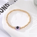 Golden beaded evil eye bracelet with purple charm and crystal spacers on a white shell tray - Purple Eye