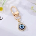 Nahaufnahme des vergoldeten Evil Eye Schlüsselanhängers mit weißen Strasssteinen und Emaille - Wassertropfenauge mit Strass