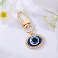 Detail eines goldenen Evil Eye Schlüsselanhängers mit blauer Emaille und funkelnden Kristallen - Ovales Auge mit Strass