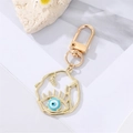 Llavero de ojo turco dorado con esmalte azul y hojas de metal sobre fondo blanco elegante - Ojo Azul Esmaltado Irregular