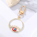 Porte-clés Evil Eye en alliage doré avec émail bleu et fermoir mousqueton sur fond blanc - Œil Rouge Rond Ajouré Cils