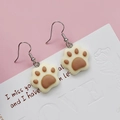 Close-up of cute white resin cat paw earrings with brown pads on a pink floral background - Brown Cat Paw