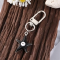Llavero de estrella con esmalte negro y ojo turco sobre fondo de madera rústica - Estrella Tono Plateado Esmalte (K200)