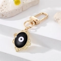 Detail showing the golden evil eye pendant with embossed floral edges on a metal keychain - Oval Black Enamel (K200)