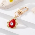 Primer plano del llavero ojo de la suerte rojo con encaje dorado sobre fondo de piedra - Gota de Agua Esmalte Rojo (K200)