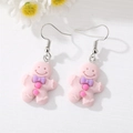 Détail de boucles d'oreilles bonhomme pain d'épice en résine rose avec nœud violet mat - Bonhomme de Pain d'Épice Rose Clair