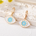 Detail of bohemian gold Evil Eye hoop earrings with blue enamel on a white textured stand - Ear Buckle / Blue