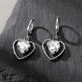 Sparkling silver heart pendant earrings with clear zircon on a dark textured stone surface - Heart Huggies