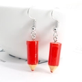 Detailed view of red pencil-shaped resin earrings hanging on a white bowl rim - Red