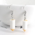 Close-up of white resin pencil-shaped earrings hanging on a white ceramic bowl - White