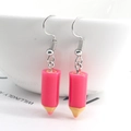 Detailed close-up of pink pencil resin earrings hanging on a white ceramic bowl edge - Rose Red