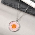 Detailed close-up of a round pink dried daisy flower pendant in transparent resin casing - Pink Petals Yellow Flower
