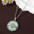 Macro detail of a clear round pendant with a real light blue dried flower on a silver chain - Blue