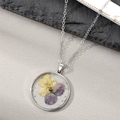 Detail of round handmade pressed dried flower pendant with silver chain and foil flakes - Pansy