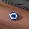 Macro shot of silver-framed evil eye charm with blue enamel layers on a stone background - Big Eye Brooch