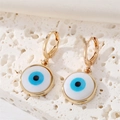 Close-up of bohemian golden evil eye hoop earrings on white stone and silk background - Round Eye