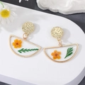 Detail von handgemachten Goldohrringen mit echten gelben Trockenblumen in Harz - Gänseblümchen