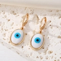 Detail of gold-plated evil eye hoop earrings with blue iris charm on white stone base - Oval Eye