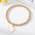 Close-up of golden beaded bracelet featuring a minimalist white smiley face charm - White Smiley Face Bracelet