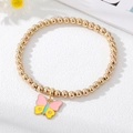 Detail of a gold beaded bracelet with a colorful enamel butterfly charm and pink stars - Yellow Butterfly Bracelet