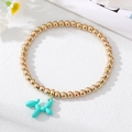 Detail of golden beaded bracelet featuring a vibrant turquoise balloon dog charm pendant - Green