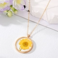 Gros plan du pendentif rond doré en résine avec une véritable fleur de marguerite jaune - Style Tournesol