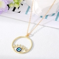 Détail du collier pendentif œil porte-bonheur doré avec cils sur une surface texturée blanche - Mauvais Œil Bleu et Vert