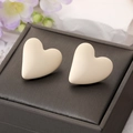 Macro shot of matte cream heart stud earrings on a textured gift box with lilac flowers - White