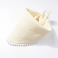 Close-up of light yellow cotton gauze baby bib with white pom-pom trim and snap button - Beige