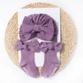 Detail of purple baby turban hat and matching socks with bow accents on a woven mat - Taro Purple