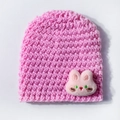 Close-up of pink knit baby beanie featuring a plush bunny embroidery with crochet texture - Pink