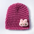Detailed knit texture of a pink winter hat featuring a cute plush bunny decoration - Dusky Pink