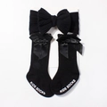Close-up of black baby socks with satin bow and matching elastic headband on white card - Black