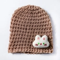 Close-up of brown knit baby hat with soft white plush bunny head and thick warm texture - Coffee