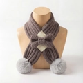 Detail of knitted baby scarf with bow and soft grey pompoms on a wooden display - Gray