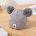 Detailed texture of grey knit baby hat with dual faux fur pom-poms and logo tag - Gray