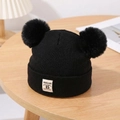 Close-up of black double pompom knitted baby hat with woven label on a wooden desk - Black