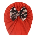Detailed view of red infant turban hat featuring a large floral bow on soft knit fabric - Orange