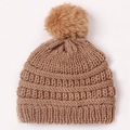 Gros plan d'un bonnet en tricot marron pour bébé avec texture épaisse et un grand pompon - Café