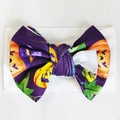 Baby headband with purple Halloween bow featuring orange pumpkin and witch hat patterns - White
