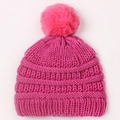 Détail d'un bonnet en tricot rose pour bébé avec texture épaisse et grand pompon moelleux - Rose rouge