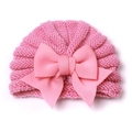 Détail d'un bonnet en tricot rose pour bébé orné d'un grand nœud en tissu sur fond blanc - Rose