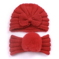Detail of red knitted baby set featuring a soft bow beanie and a faux fur pompom headband - Red