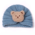 Detailed close-up of light blue knit baby turban hat with a 3D plush bear patch decoration - Blue