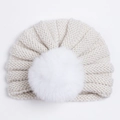 Detailopname van een gebreide babytulbandmuts met een pluizige witte pompon van imitatiebont - Broken Wit