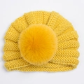 Détail d'un bonnet en tricot jaune vif pour bébé avec un grand pompon en fausse fourrure - Jaune